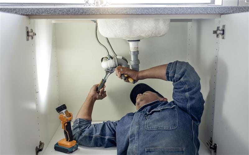 Plumber repairing pipes beneath a bathroom sink in Saratoga